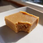 A single square of creamy peanut butter fudge with a bite taken out, showing the texture.