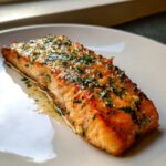 Close-up of a perfectly cooked salmon recipe fillet glazed with butter, garlic, and fresh parsley.