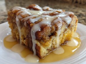 Close-up of a square slice of rich bread pudding topped with thick white icing and sitting in a pool of caramel sauce.