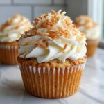 A close-up of one amazing coconut cupcake topped with white frosting and toasted coconut flakes.