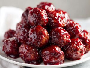 A close-up pile of juicy cranberry meatballs coated in a thick, glossy, dark red cranberry sauce.