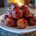 A close-up stack of glistening cranberry meatballs coated in a rich, dark red sauce on a white plate.