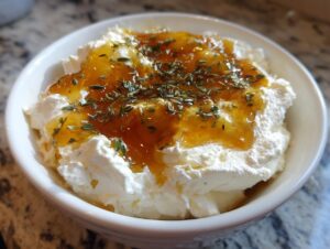 Close-up of a bowl filled with creamy ricotta dip, drizzled with amber honey and sprinkled with fresh thyme.