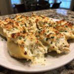 Close-up of baked chicken alfredo stuffed shells overflowing with creamy filling and browned cheese, garnished with parsley.