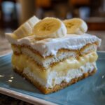 A rich slice of layered banana pudding featuring vanilla wafers, creamy pudding, whipped topping, and fresh banana slices.