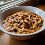 Close-up of a white bowl filled with rich, creamy cream cheese chicken chili featuring shredded chicken and dark kidney beans.