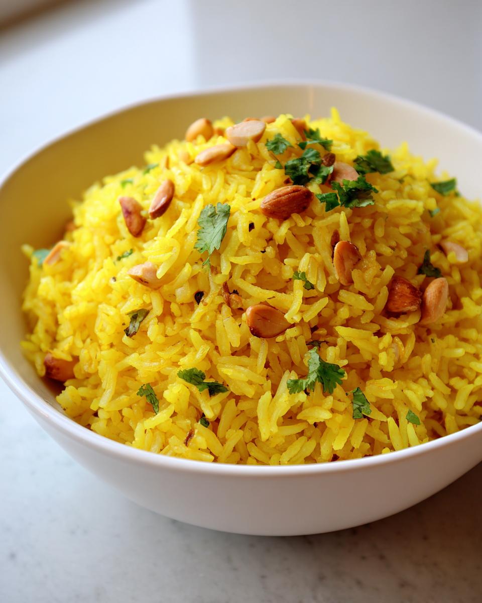 Close-up of bright yellow mediterranean rice topped with toasted almonds and fresh cilantro in a white bowl.