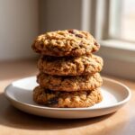 A tempting stack of four soft, chewy oatmeal raisin cookies resting on a small white plate.