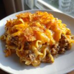 A serving of cheesy cheeseburger casserole featuring ground beef, egg noodles, and a crispy potato chip topping.