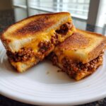 A cheesy texas toast sloppy joes sandwich cut in half, showing melted cheese and savory meat filling on grilled bread.