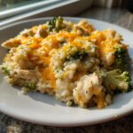 A serving of creamy chicken broccoli rice casserole topped with melted cheddar cheese on a white plate.
