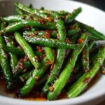 Close-up of bright green, glossy chinese green beans with garlic sauce coating them.