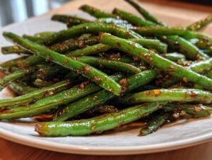 A close-up shot of vibrant, glossy chinese green beans with garlic sauce piled on a white plate.