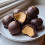A pile of rich chocolate-covered peanut butter balls, with two cut in half showing the creamy center.
