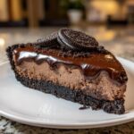 A decadent slice of chocolate mousse pie with a dark crust, topped with chocolate ganache and Oreo cookies.