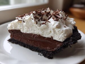 A perfect slice of rich Christmas chocolate cream pie featuring a dark crust, thick chocolate filling, and generous whipped cream topping.