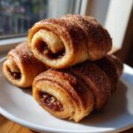 A close-up stack of golden brown Rugelach pastries coated in cinnamon sugar, showing the dark fruit filling inside.
