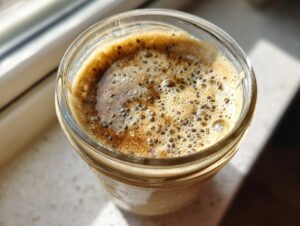 Overhead view of coffee overnight oats in a glass jar topped with foam and visible chia seeds.