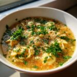 Close-up of a white bowl filled with hot pastina soup, garnished generously with fresh parsley and grated cheese.