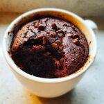 Close-up of a fudgy Cottage Cheese Microwave Brownie baked in a white mug, topped with chocolate chips.