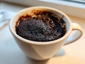 Close-up of a rich, dark chocolate Cottage Cheese Microwave Brownie baked inside a white mug.