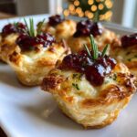 Close-up of baked cranberry brie bites in puff pastry cups, topped with cranberry sauce and rosemary.