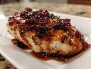 Close-up of a perfectly cooked cranberry chicken breast topped with a rich, glossy cranberry glaze.