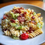 Close-up of a creamy blt pasta salad featuring rotini pasta, cherry tomatoes, lettuce, and crispy bacon crumbles.
