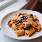A serving of creamy butternut squash pasta featuring large tube pasta, topped with fried sage leaves and grated Parmesan cheese.