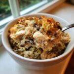 Close-up of a spoonful of creamy chicken and wild rice casserole with a golden, crispy topping.