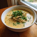 A white bowl filled with creamy chicken poblano soup, topped with shredded chicken and fresh cilantro.
