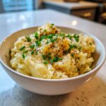 A white bowl filled with creamy garlic mashed potatoes, topped generously with fresh chives and cracked black pepper.