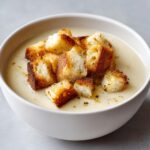 A close-up of creamy garlic soup topped generously with golden, toasted croutons.