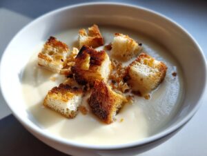 Close-up of creamy white garlic soup topped with golden brown, toasted croutons.