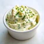 A small white bowl filled with creamy horseradish sauce mixed with fresh green chives.
