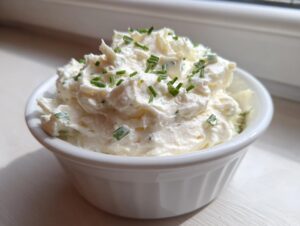 A small white bowl filled with creamy horseradish sauce, garnished with fresh chopped chives.