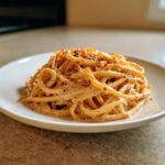 A close-up of creamy parmesan pasta served on a white plate and sprinkled with red pepper flakes.