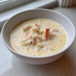A white bowl filled with creamy she crab soup, generously topped with shredded crab meat and a sprinkle of paprika.