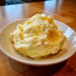 A generous serving of creamy, fluffy slow cooker mashed potatoes piled high in a small white bowl.