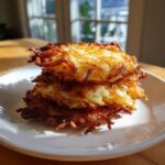 A stack of three perfectly golden brown and crispy potato latkes served on a white plate.