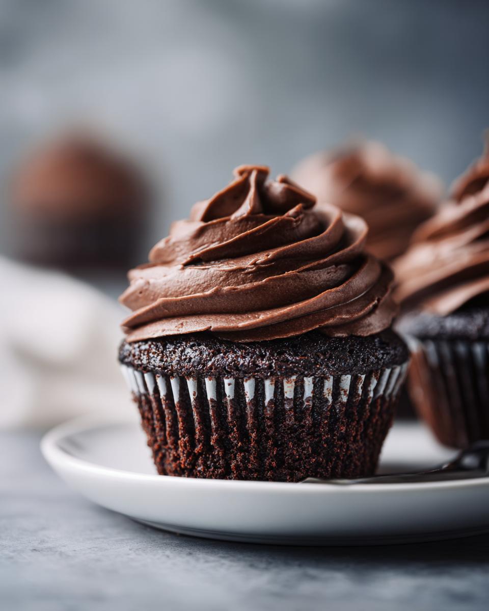 A close-up of one perfect easy chocolate cupcakes topped with a swirl of dark chocolate frosting on a white plate.