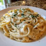 Close-up of fettuccine pasta generously coated in creamy Olive Garden Alfredo Sauce, topped with parsley.