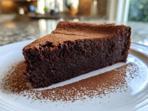 A decadent slice of flourless chocolate torte dusted generously with cocoa powder, served on a white plate.