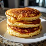 A tall stack of three golden-brown, fluffy buttermilk pancakes sitting on a white plate.