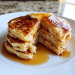 A thick stack of fluffy old fashioned pancakes, cut open to show the texture, topped with melting butter and dripping with syrup.