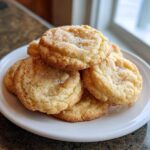 A stack of golden french salted butter cookies sprinkled with coarse sugar crystals on a white plate.