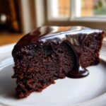 Close-up of a rich, dark slice of flourless chocolate cake topped with glossy, dripping chocolate ganache.