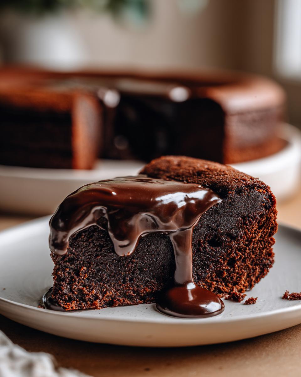 A rich slice of flourless chocolate cake topped with thick, glossy chocolate ganache dripping down the side.