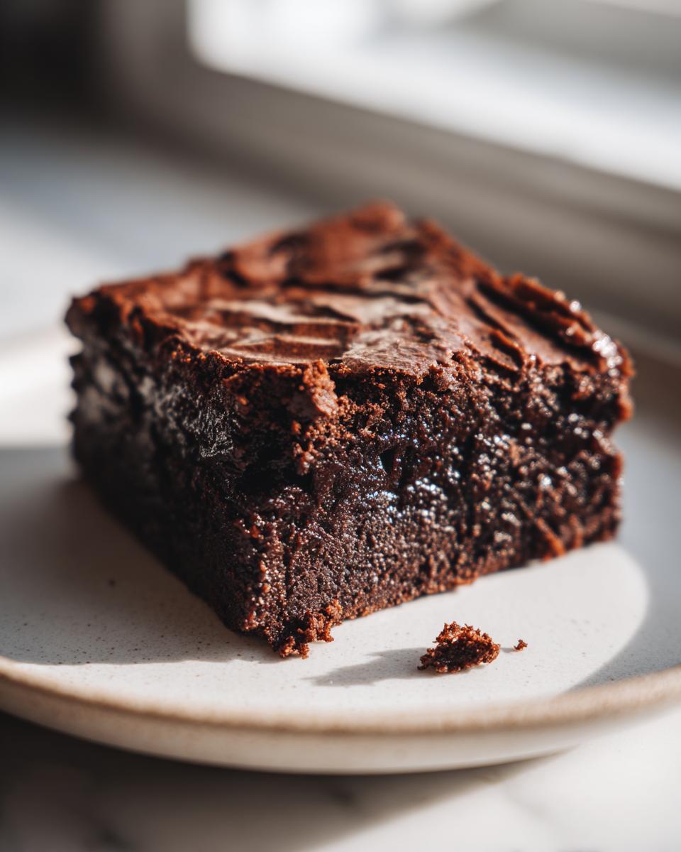 Close-up of a single, fudgy slice of sweet potato brownies with a shiny top, resting on a light plate.