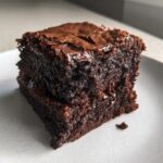 Two stacked, dark, fudgy squares of sweet potato brownies with a shiny, cracked top.